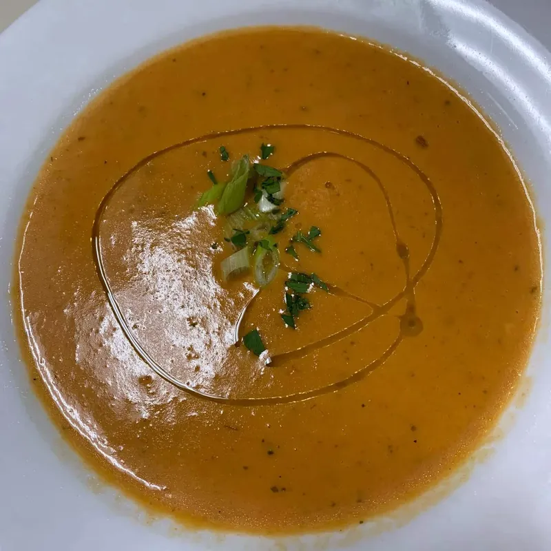 Bowl of orange soup with a swirl of olive oil and herbs