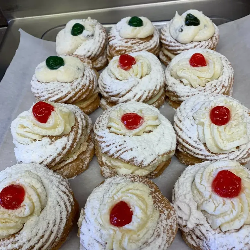 Tray of zeppole dusted with powdered sugar and topped with cherries