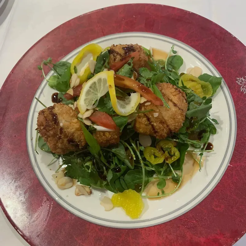 Breaded cakes on arugula with lemon and peppers on a red-rimmed plate