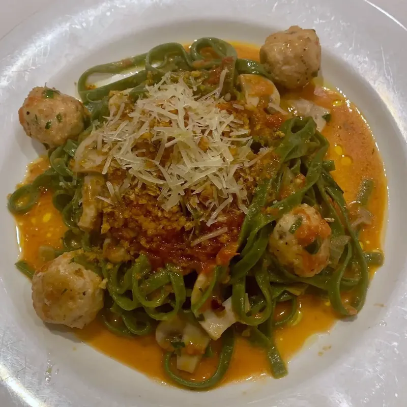 Green pasta with shrimp and small meatballs in orange sauce